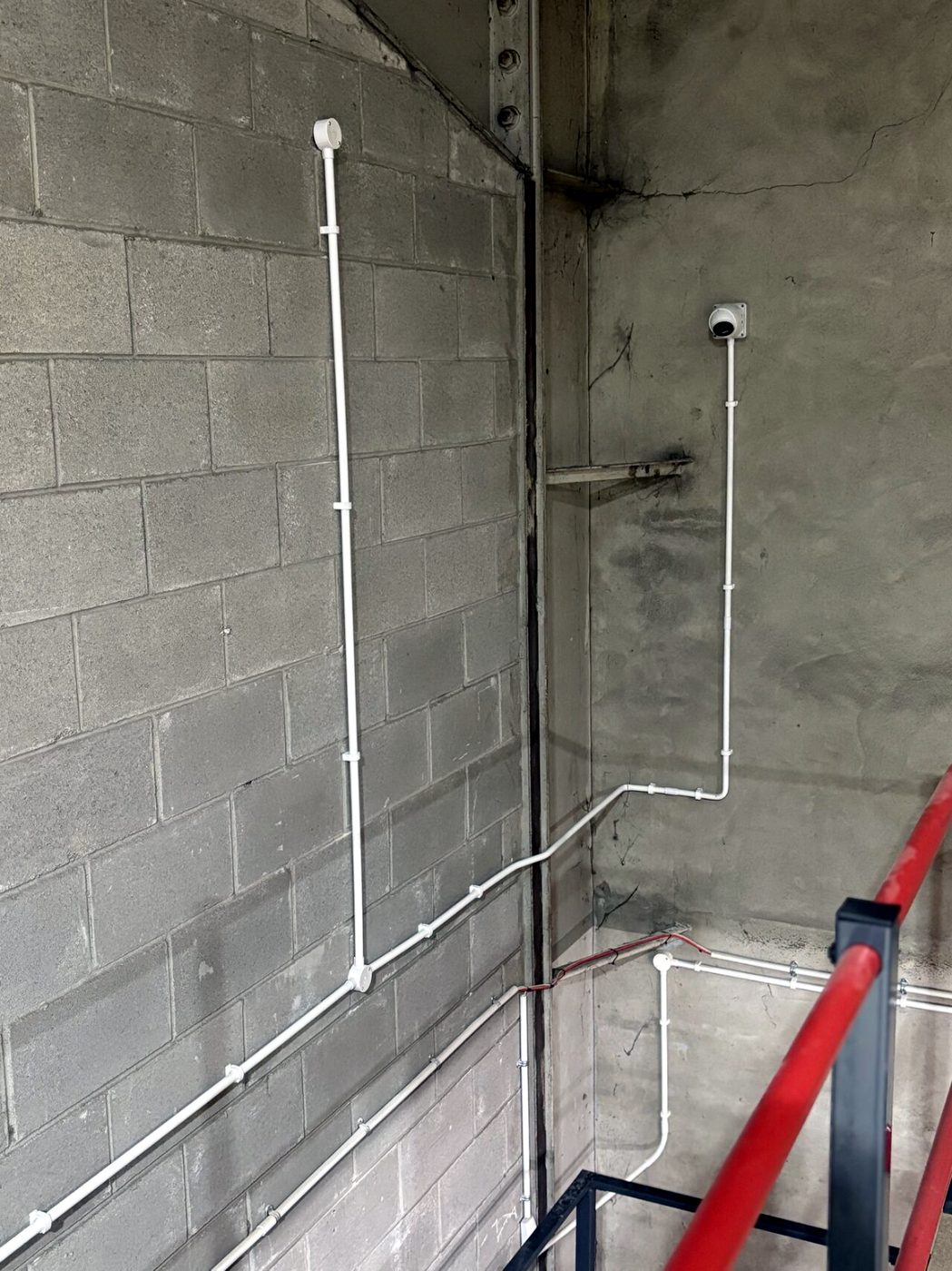 Neatly clipped white conduit and camera cabling running down a stairwell wall