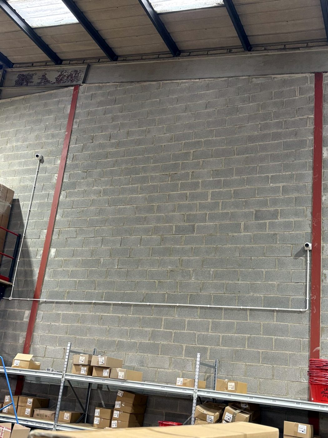 Two ORR-installed CCTV cameras covering a warehouse wall with neatly run surface conduit